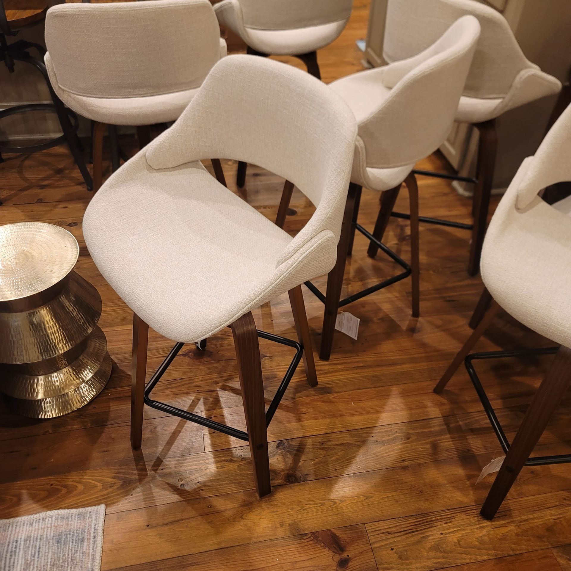 Group of modern beige bar stools with wooden legs and curved backrests on a polished hardwood floor.