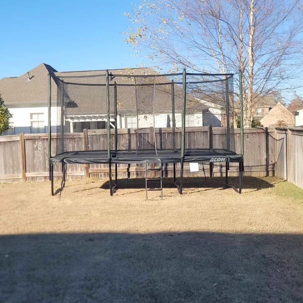 Trampoline with safety netting set up in a fenced backyard on a sunny day.